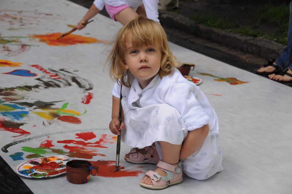 The picture shows a small girl painting on the pavement